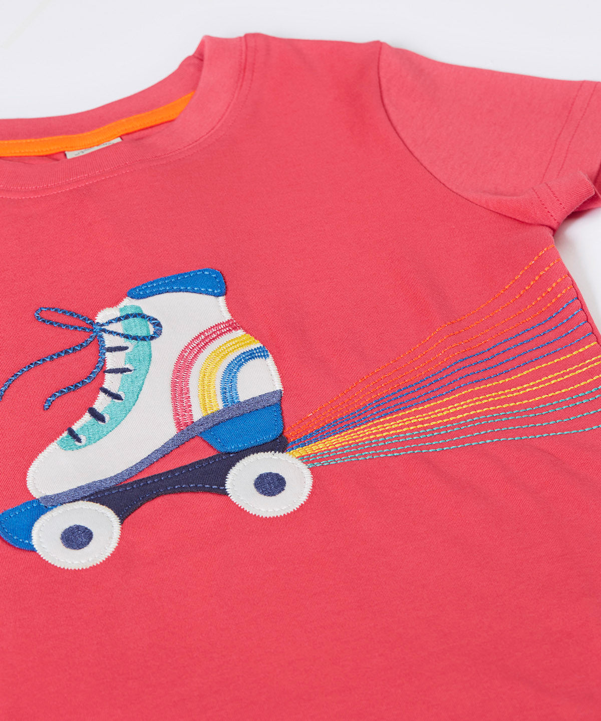 A close up of the Frugi t-shirt laid flat showing the white and blue roller blade appliqué against light pink fabric