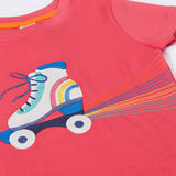 A close up of the Frugi t-shirt laid flat showing the white and blue roller blade appliqué against light pink fabric
