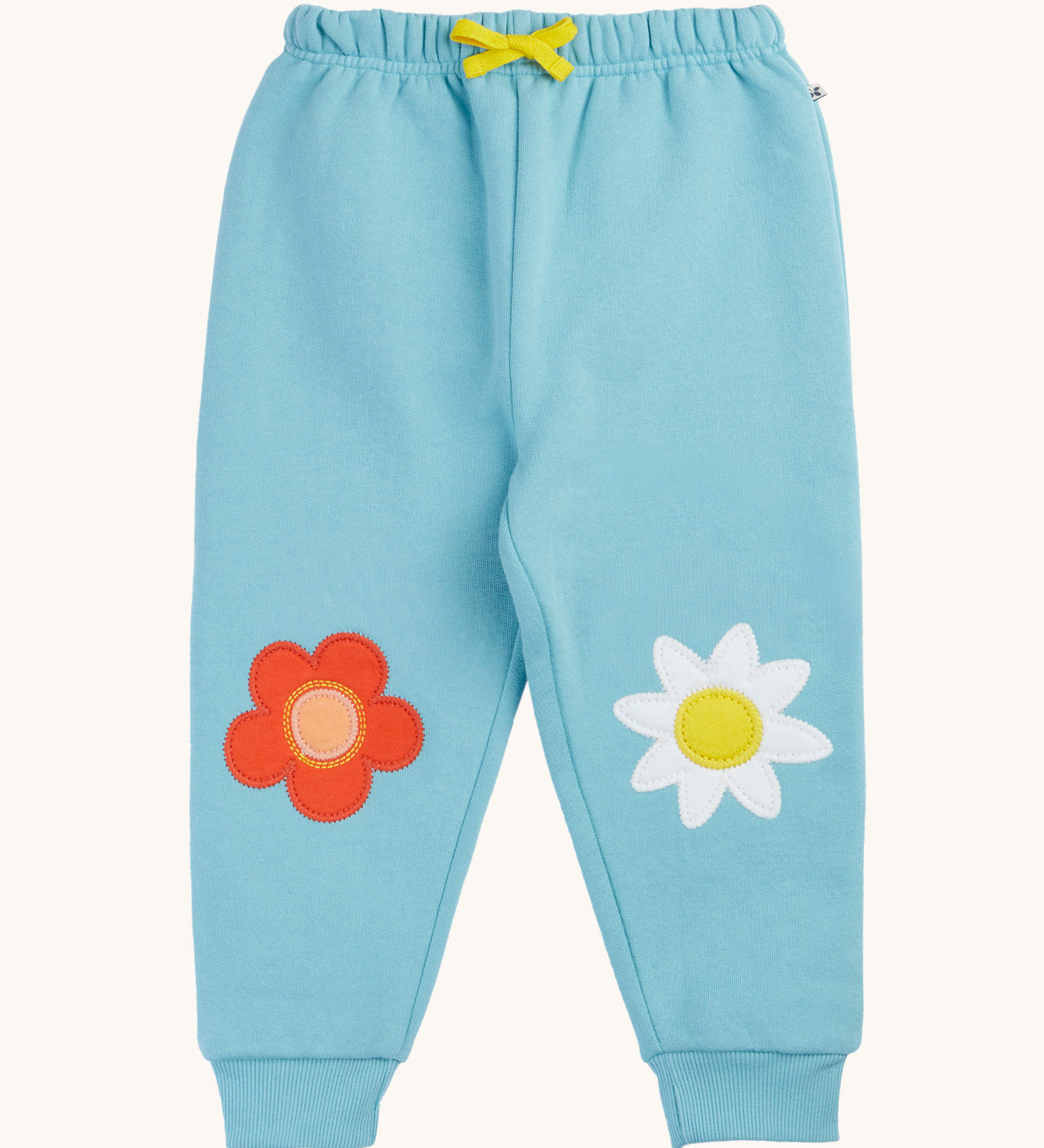 Frugi organic cotton joggers laid flat. In light blue with a red flower applique on one knee and a white flower on the other knee. Features a yellow tie on the waist band