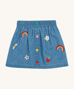 Frugi kids denim skirt with a flower, rainbow and strawberry design on a cream background.