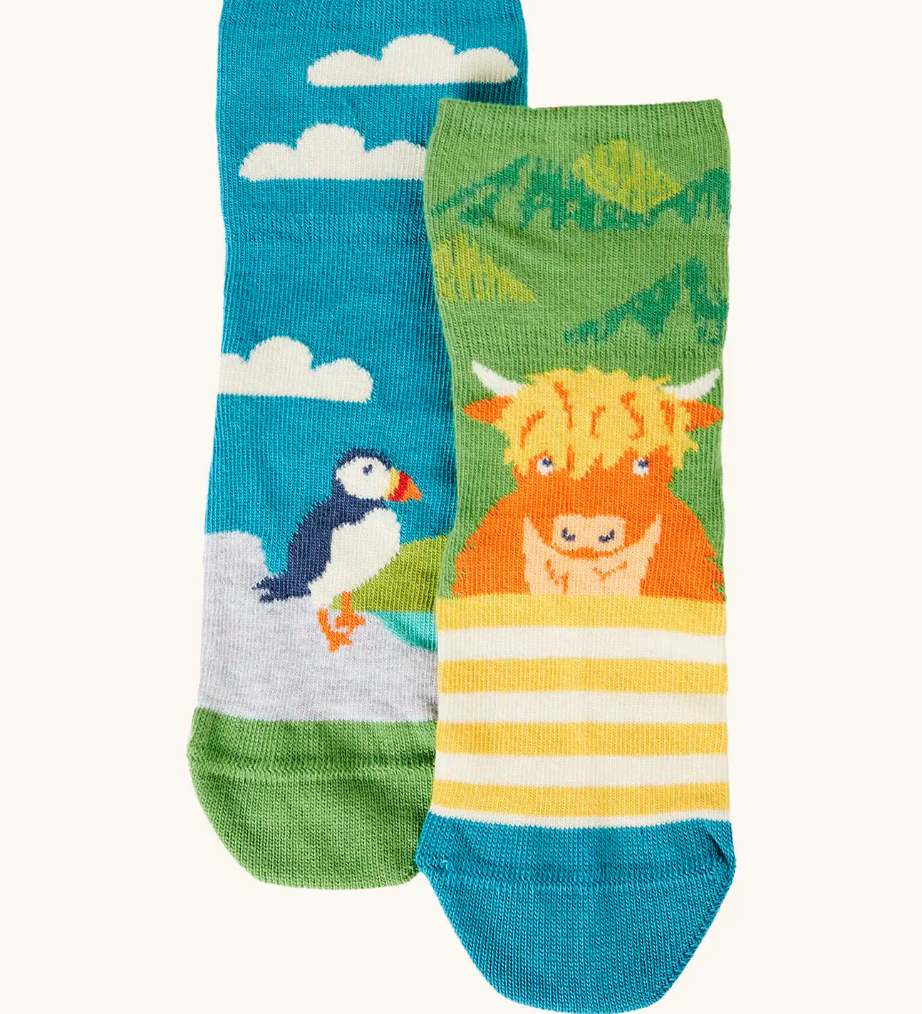 Frugi GOTS organic cotton socks 2 pack  One pair with yellow stripes with a little Highland cow other has a blue sky landscape with a puffin with details hidden under the cuff