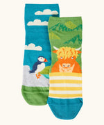 Frugi GOTS organic cotton socks 2 pack  One pair with yellow stripes with a little Highland cow other has a blue sky landscape with a puffin with details hidden under the cuff