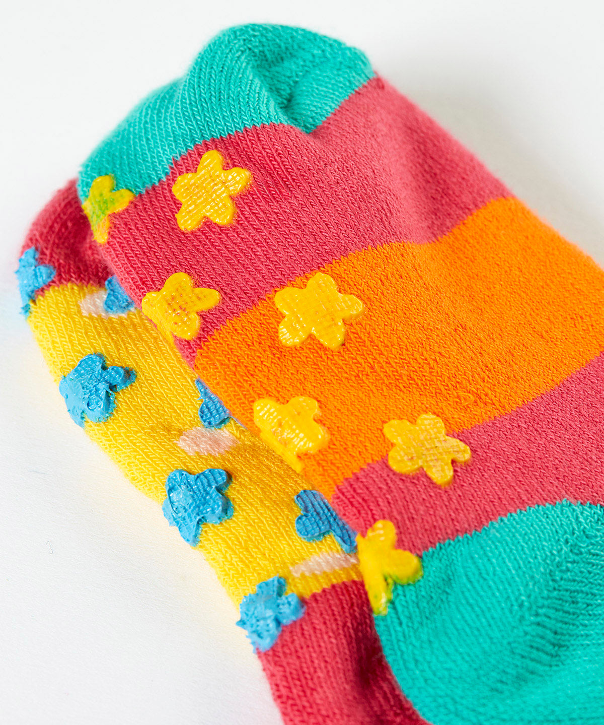 A close up of the underside of the Frugi organic cotton 2 pack socks laid flat. In bright striped colours with little star grip panels