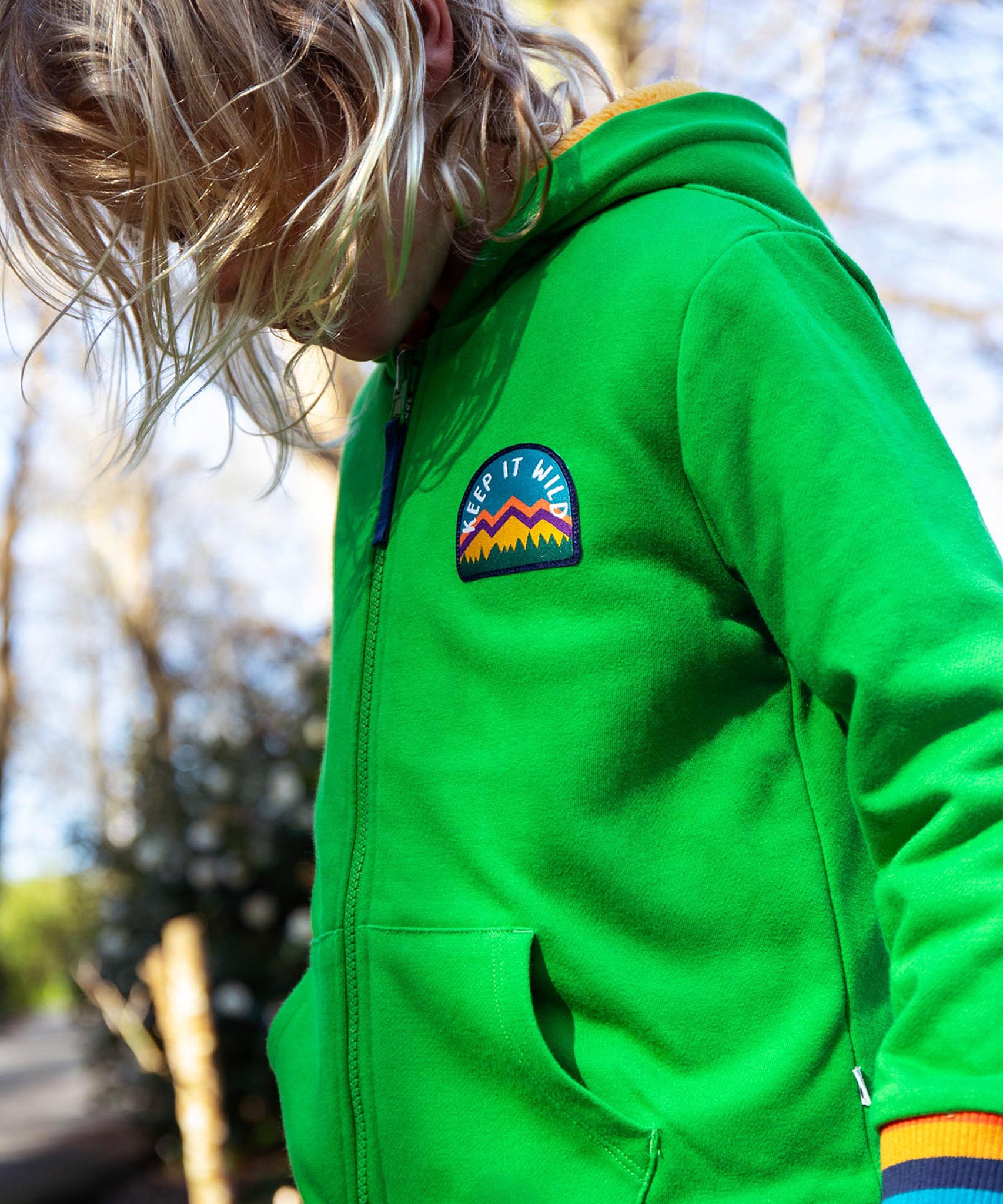 A child standing outside and wearing the green Jersey style Frugi helston reversible hoodie.