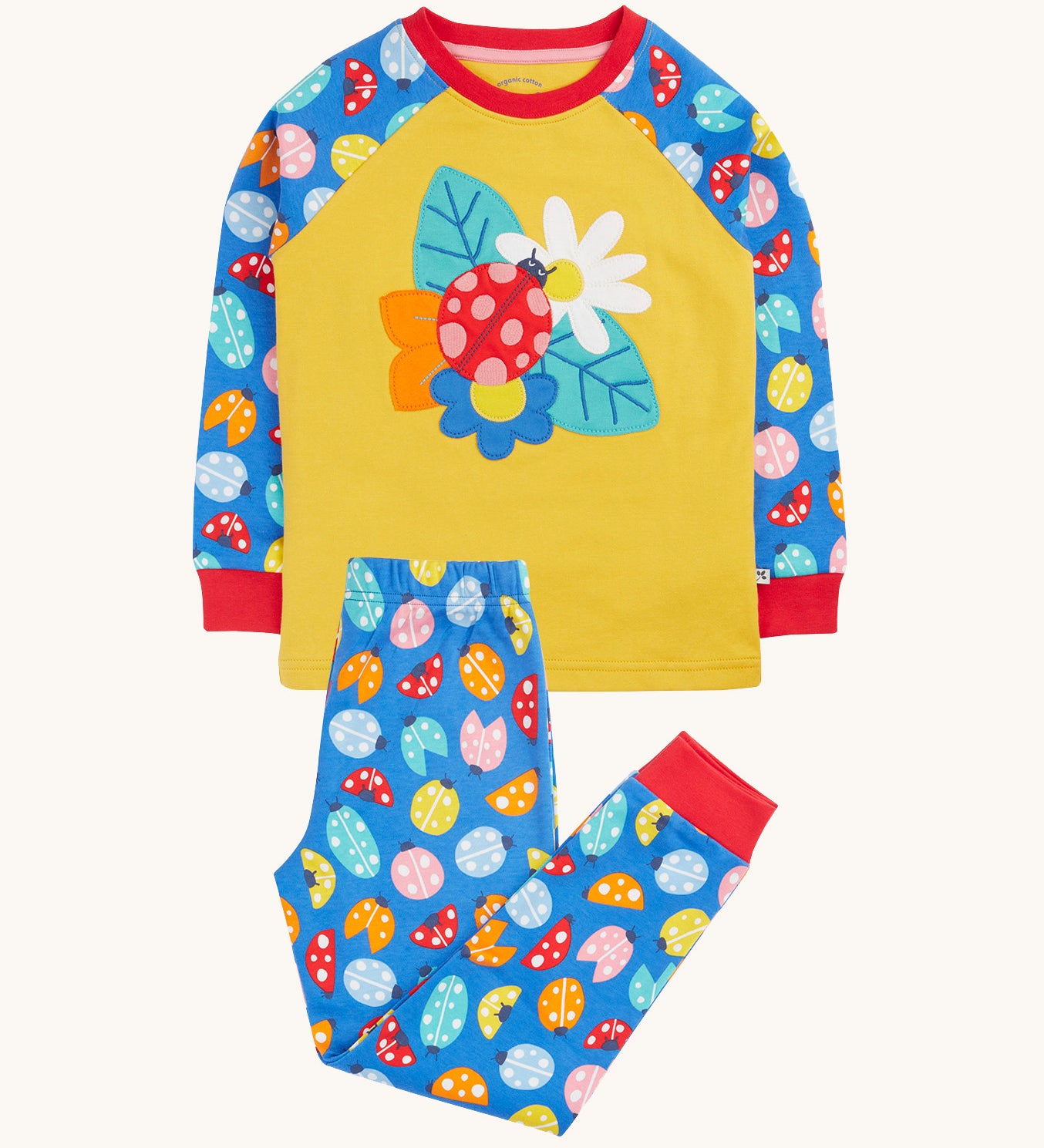 Frugi organic cotton pyjama set laid flat. A mustard yellow top with a ladybird design on the front and blue sleeves with a repeating ladybird design. Trousers in the same blue and the repeating ladybird print