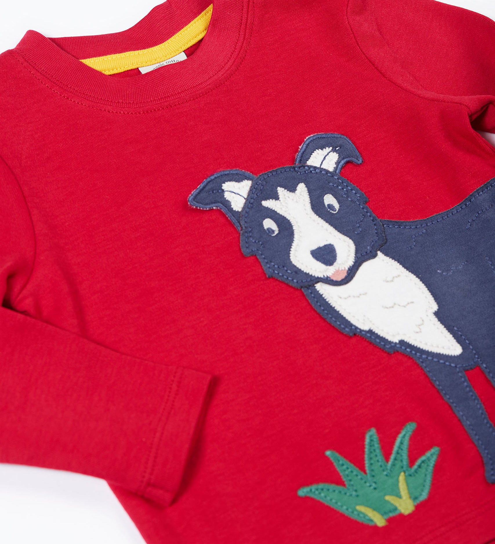 A close up of the Frugi kids adventure applique top berry red/sheepdog top showing the sheepdog applique and popper detail on red organic cotton fabric.