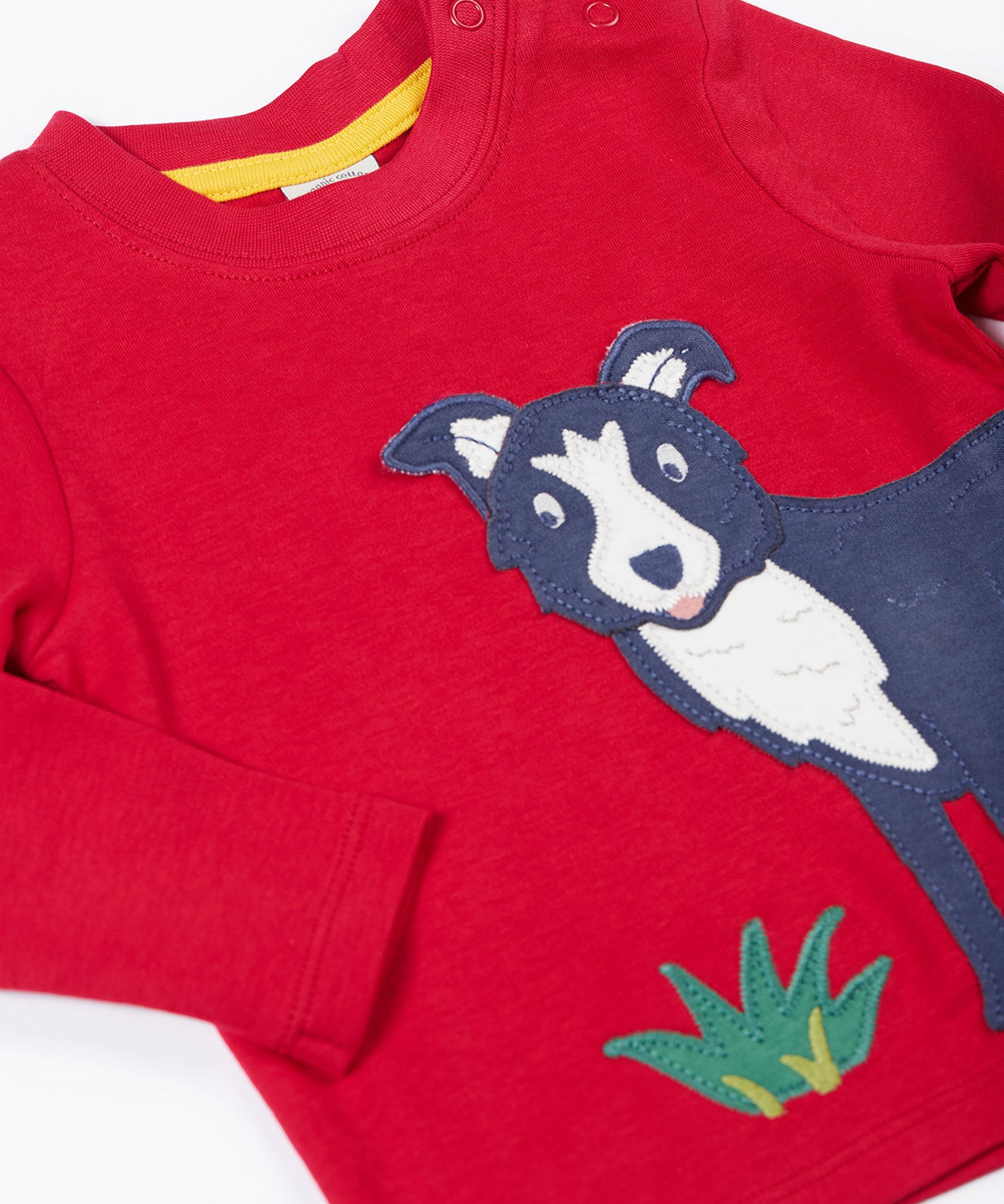 A close up of the Frugi kids adventure applique top berry red/sheepdog top showing the sheepdog applique and popper detail on red organic cotton fabric.