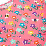 A close up of the Frugi kids bryher top in tulip fun flowers showing the playful bee and flower print detail on pink GOTs organic cotton fabric. 