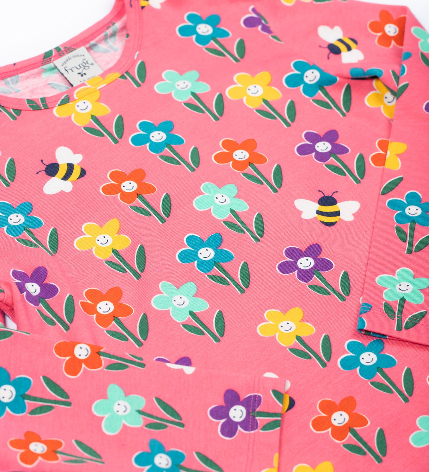 A close up of the Frugi kids bryher top in tulip fun flowers showing the playful bee and flower print detail on pink GOTs organic cotton fabric. 