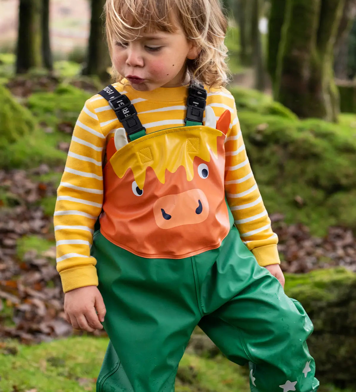 Small child wearing the Frugi water proof holly green/cow character puddle buster in the forest