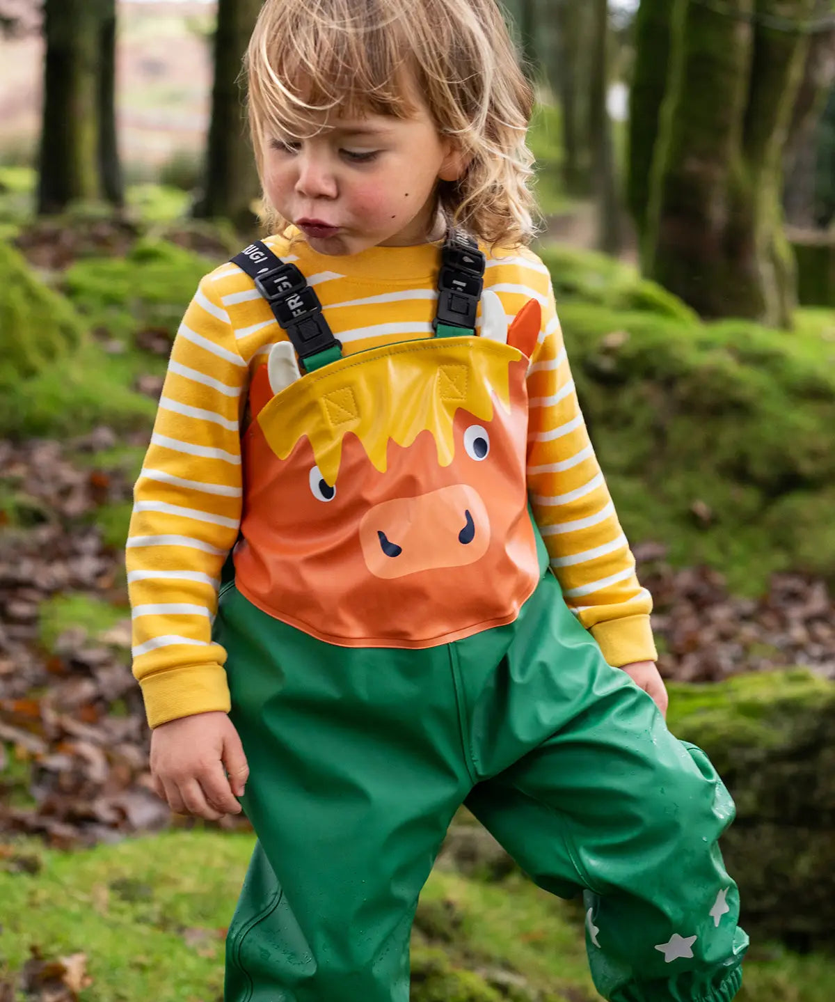 Small child wearing the Frugi water proof holly green/cow character puddle buster in the forest