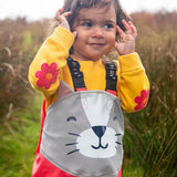 Small child wearing the Frugi character puddle buster trousers in rhubarb pink with a grey cat upper body panel