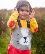Small child wearing the Frugi character puddle buster trousers in rhubarb pink with a grey cat upper body panel