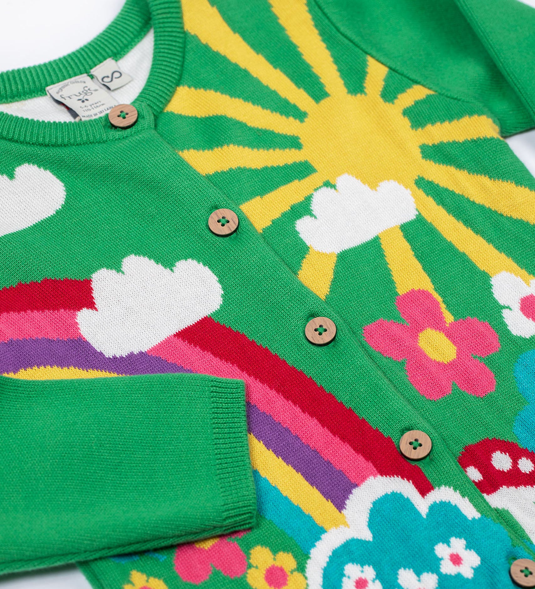 A close up of the Frugi kids corin knitted cardigan in clover/rainbow. Showing the button fastener detail on green organic cotton fabric.
