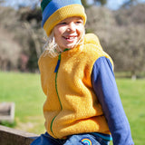 A child sitting outside and wearing the yellow ted fleece Frugi helston reversible hoodie.