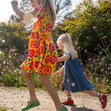 Child wearing Frugi's yellow spring skater dress with repeating bright floral designs and skipping on a path next to another child