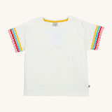 Frugi kids white short sleeve t-shirt with a rainbow trim on the sleeve on a cream background.
