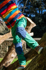 A child standing on a tree and wearing the Frugi Wilderness green trousers with navy blue coloured knee patches available at Babipur