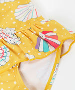 A close up of the Frugi yellow swim suit laid flat showing the repeating white shell design and frill detail on the waist.