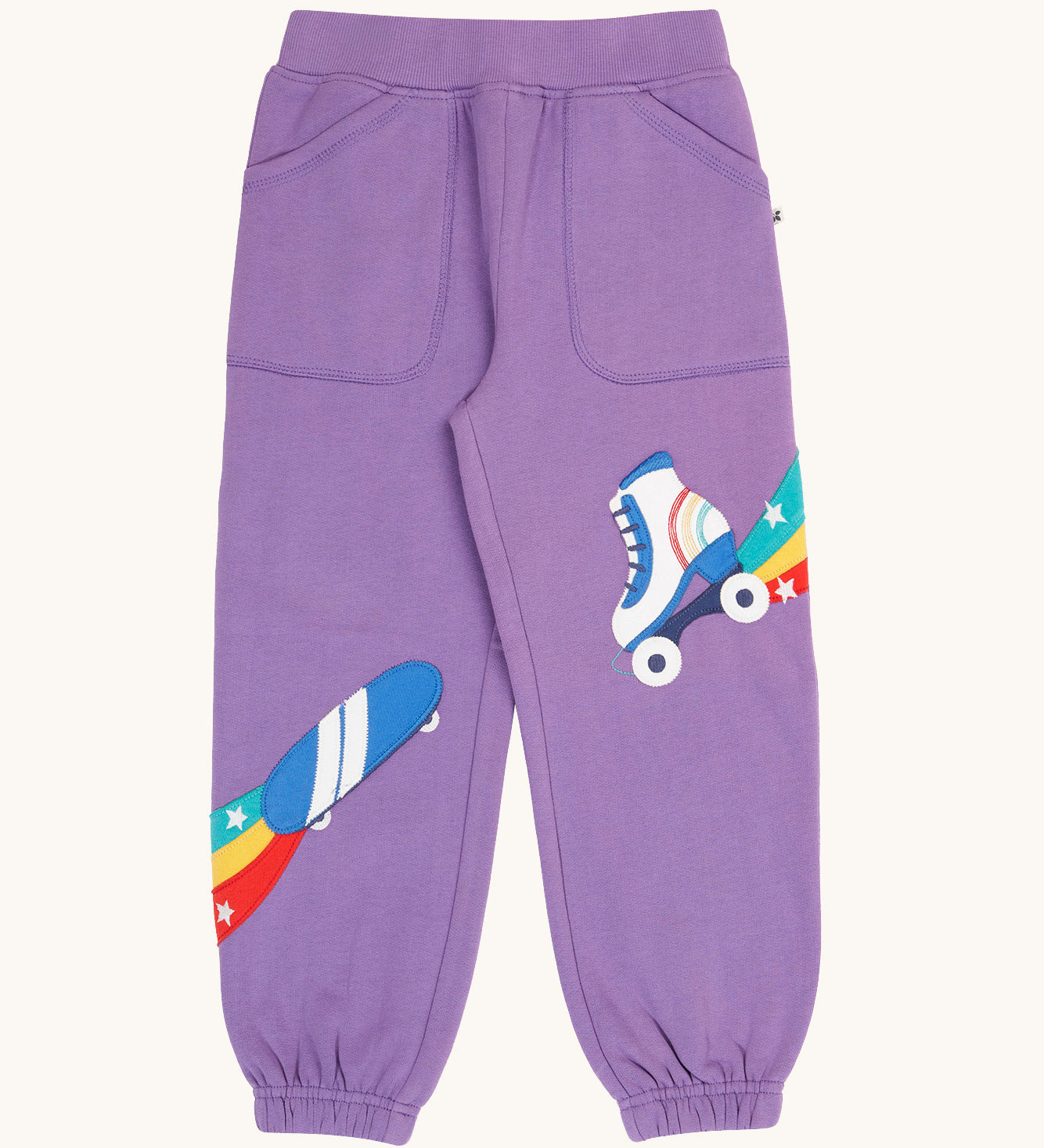 Frugi organic cotton joggers laid flat. In light purple with an skating theme applique on each leg