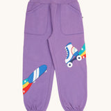 Frugi organic cotton joggers laid flat. In light purple with an skating theme applique on each leg