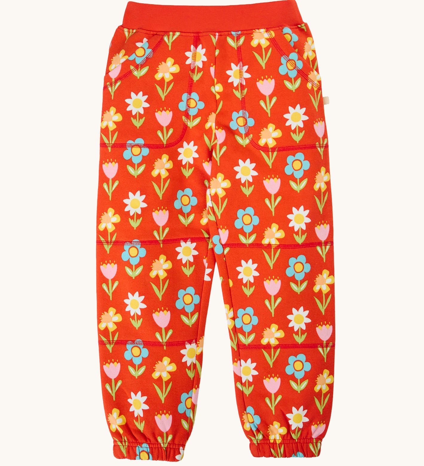 Frugi organic cotton joggers laid flat. In red with a repeating flower print and side pockets.