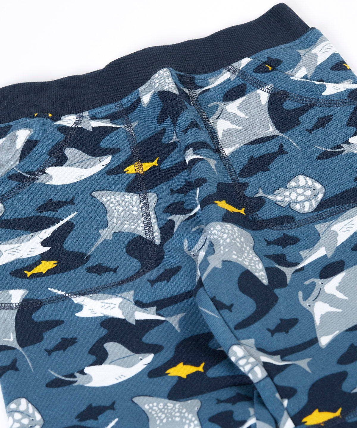 A close up of the frugi joggers laid flat showing repeating grey manta ray print and the navy elasticated waist band