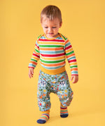 Toddler standing against a light orange background, wearing a bold striped long sleeve top, socks and the repeated farm inspired print parsnip pants