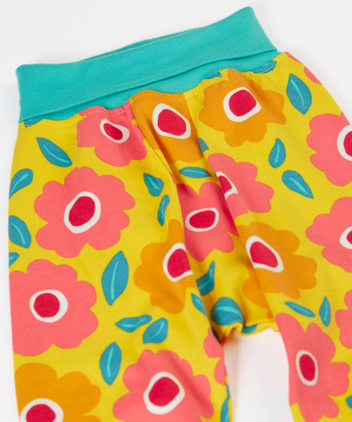 A close up of the repeating floral print and turquoise waist band on the bright yellow pants