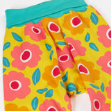 A close up of the repeating floral print and turquoise waist band on the bright yellow pants