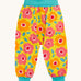 Frugi organic cotton parsnip pants laid flat. In bright yellow with a turquoise waist band and leg cuffs. Has a repeating floral print. 