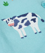 A close up of a black and white cow design on the light blue Frugi dungaree 