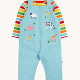 Frugi light blue organic cotton dungaree with farm animals on the front with a rainbow striped long sleeve top underneath as an outfit