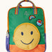 Frugi backpack standing upright. A green and orange block coloured backpack with a smiley face as a front pocket. Features a rainbow handle and patches. 