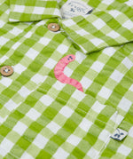 Close up of the Frugi Reggie kids shirt. showing the worm embroidery on the front pocket on green gingham organic cotton fabric
