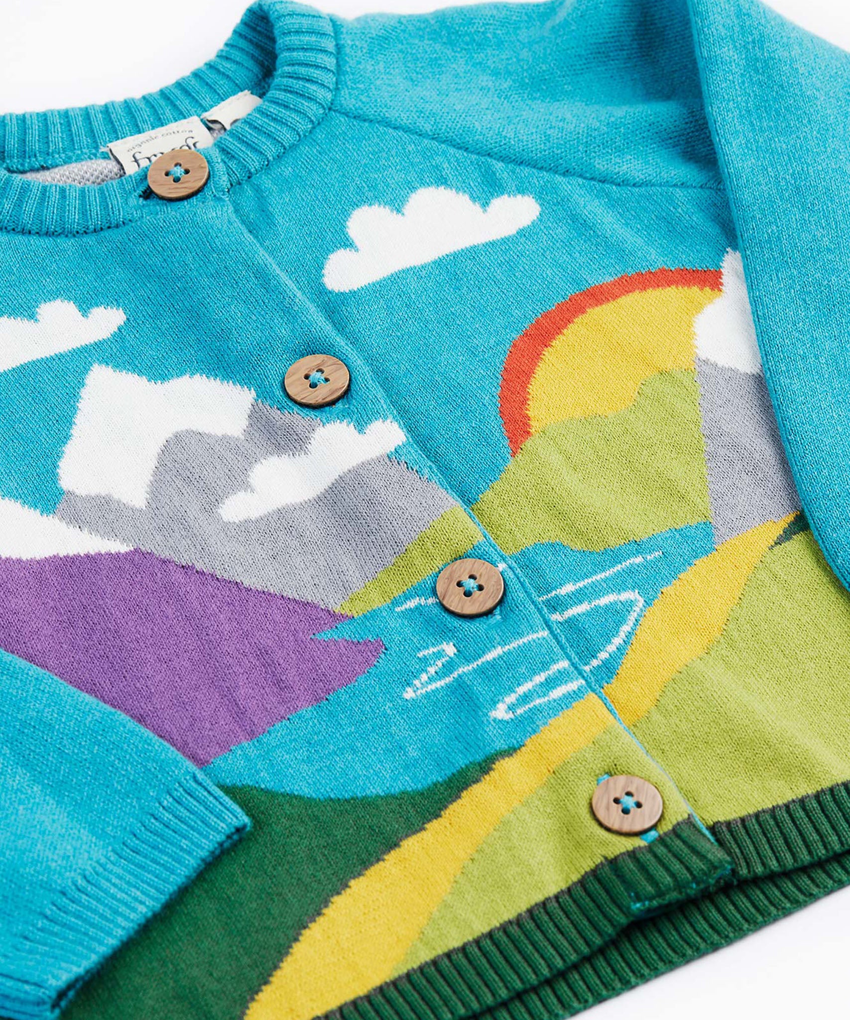 A close up of the Frugi kid reva knitted cardigan in blue/mountain scene showing the mountain scene detail and button  fasteners. 
