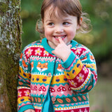 A child leaning on a tree and wearing the Frugi kids robyn fairisle cardigan in fox. A 100% GOTS organic cotton cardigan with a bright woodland fairisle design. 