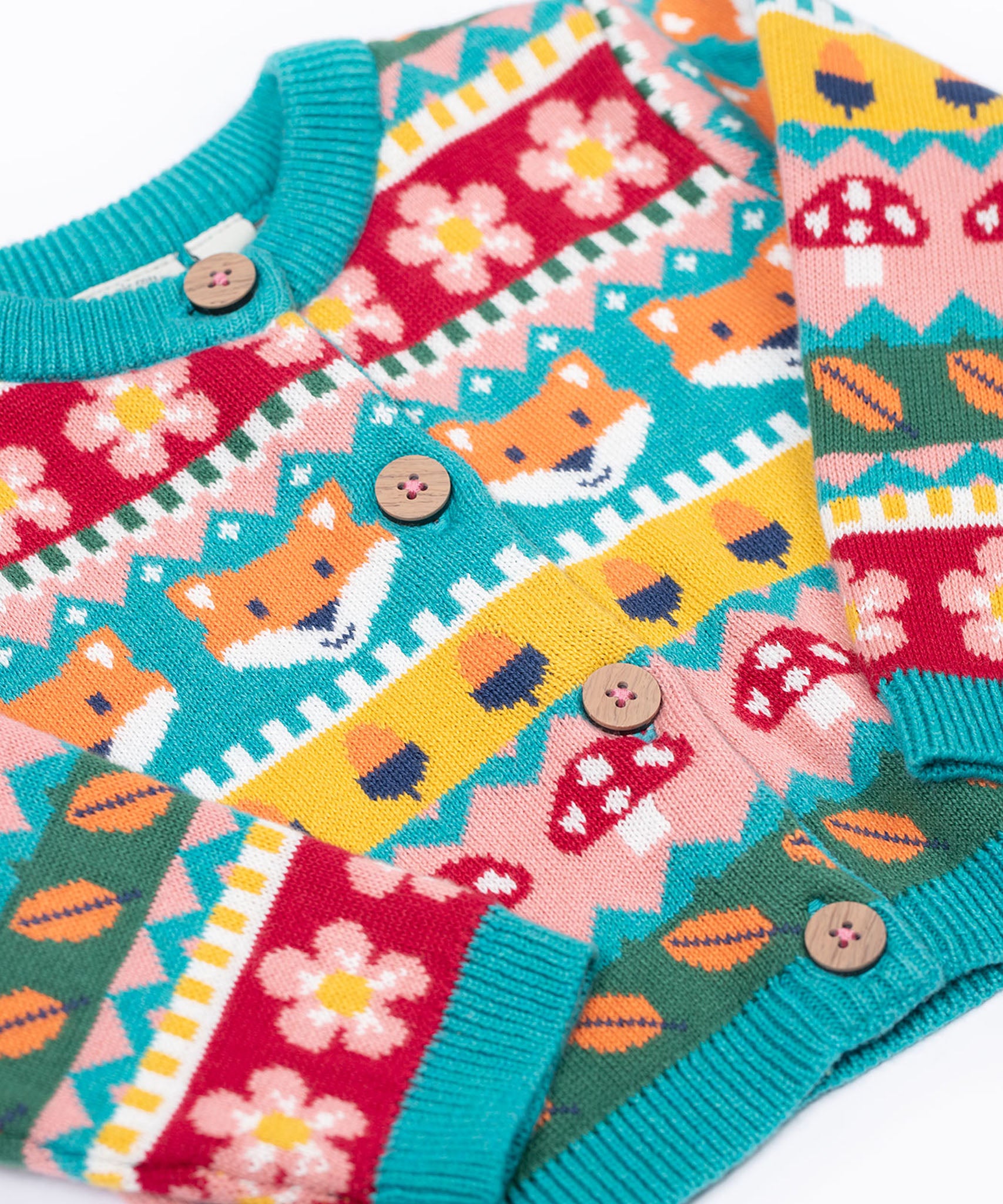 A close up of the Frugi kids robyn fairisle cardigan in fox showing the button detail and bright blue trim detail on organic cotton fabric.