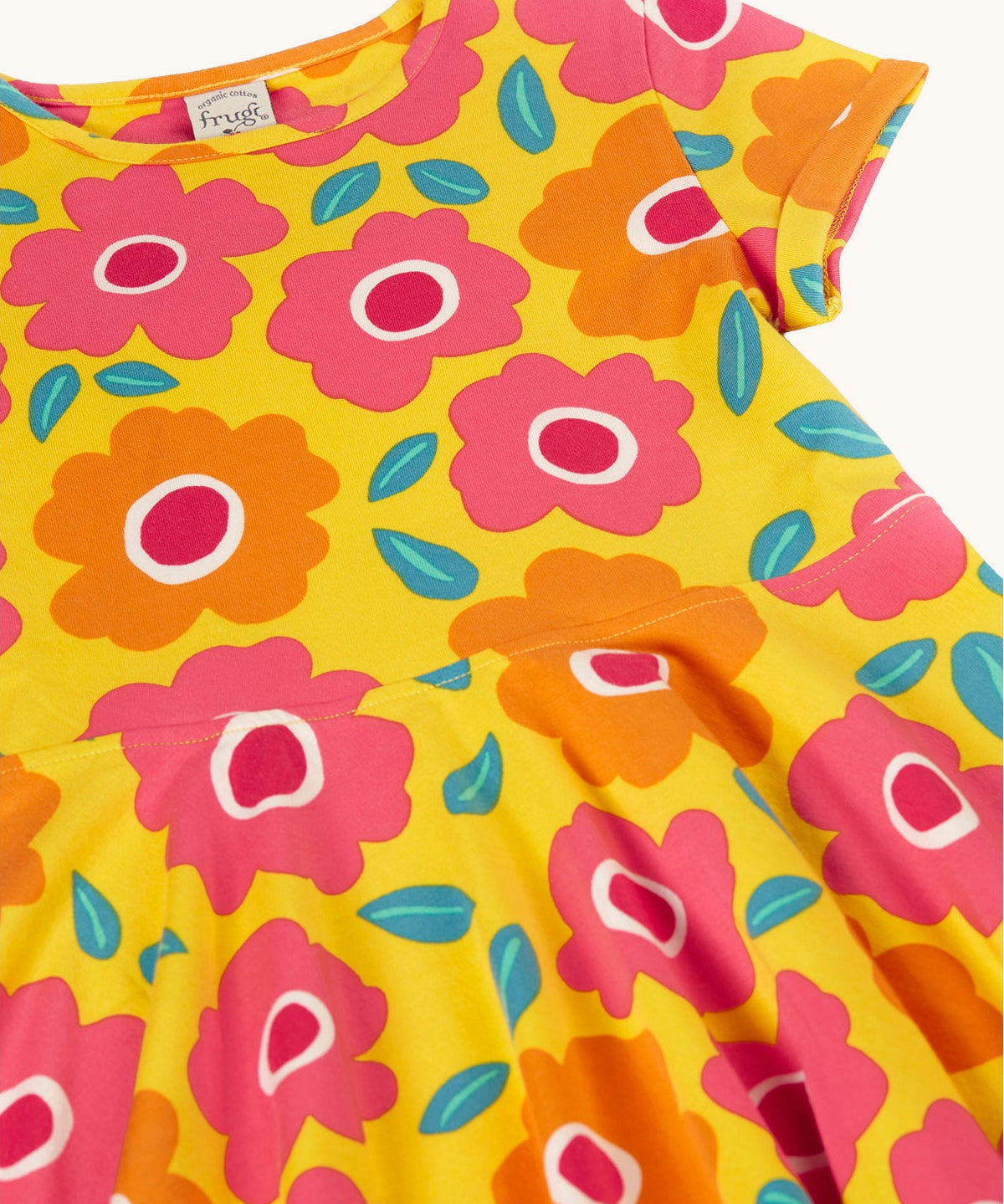 A close up of the yellow Frugi skater dress laid flat showing a repeating pink and orange floral print