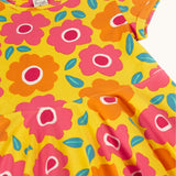 A close up of the yellow Frugi skater dress laid flat showing a repeating pink and orange floral print