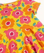 A close up of the yellow Frugi skater dress laid flat showing a repeating pink and orange floral print