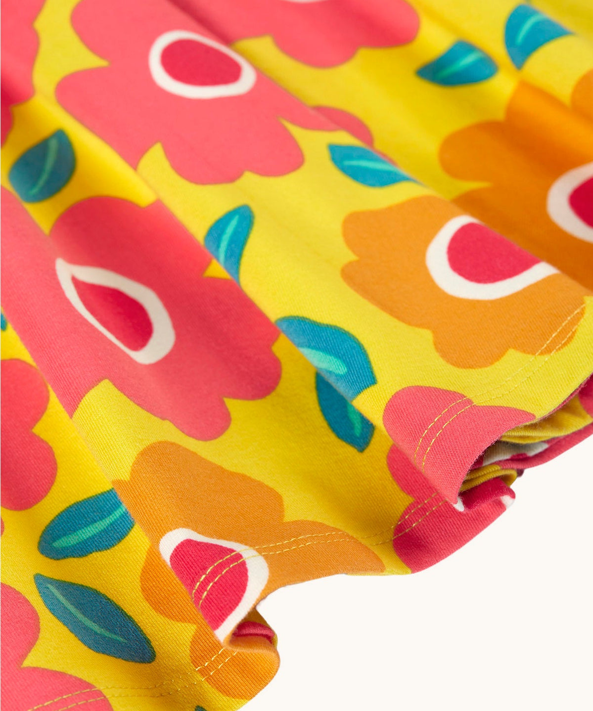 A close up of the yellow Frugi skater dress laid flat showing the frill detail and repeating floral print