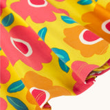 A close up of the yellow Frugi skater dress laid flat showing the frill detail and repeating floral print