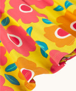 A close up of the yellow Frugi skater dress laid flat showing the frill detail and repeating floral print