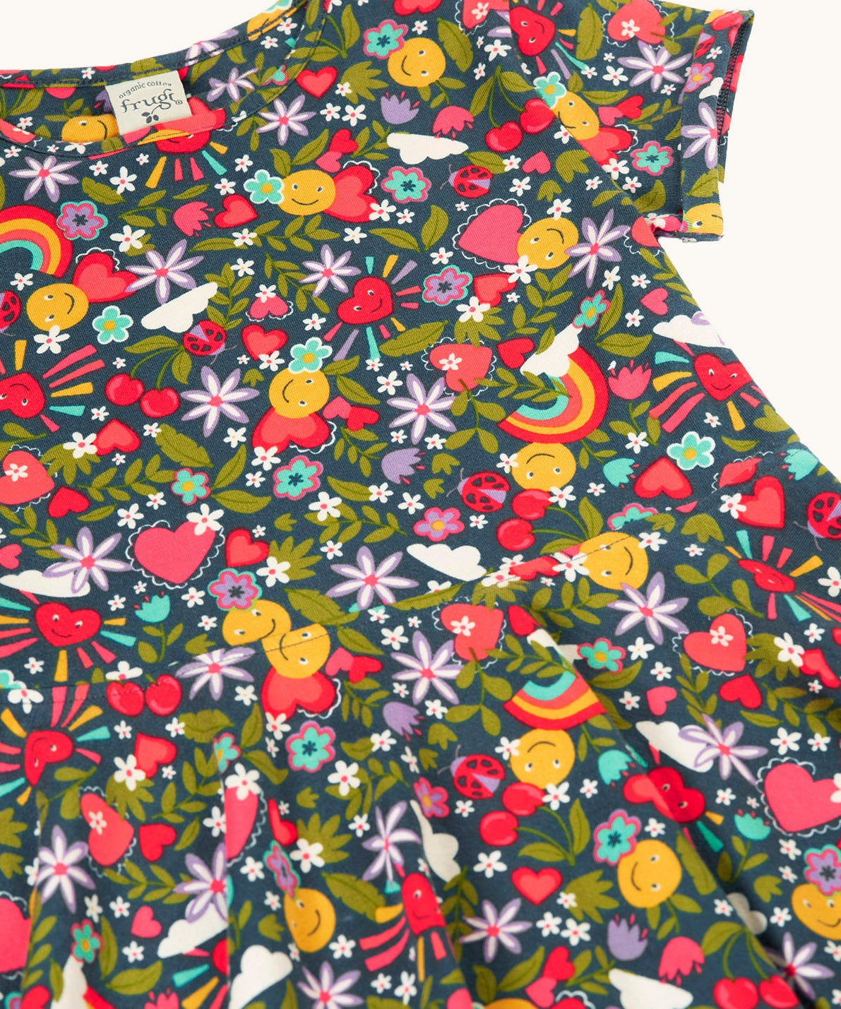 A close up of the navyFrugi organic cotton skater dress laid flat  showing the repeating heart, sun rainbow and flower print.