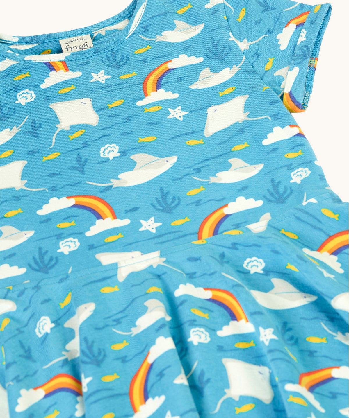 A close up of the light blue Frugi skater dress laid flat showing the repeating grey manta ray and rainbow print