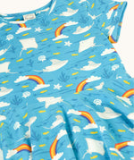 A close up of the light blue Frugi skater dress laid flat showing the repeating grey manta ray and rainbow print