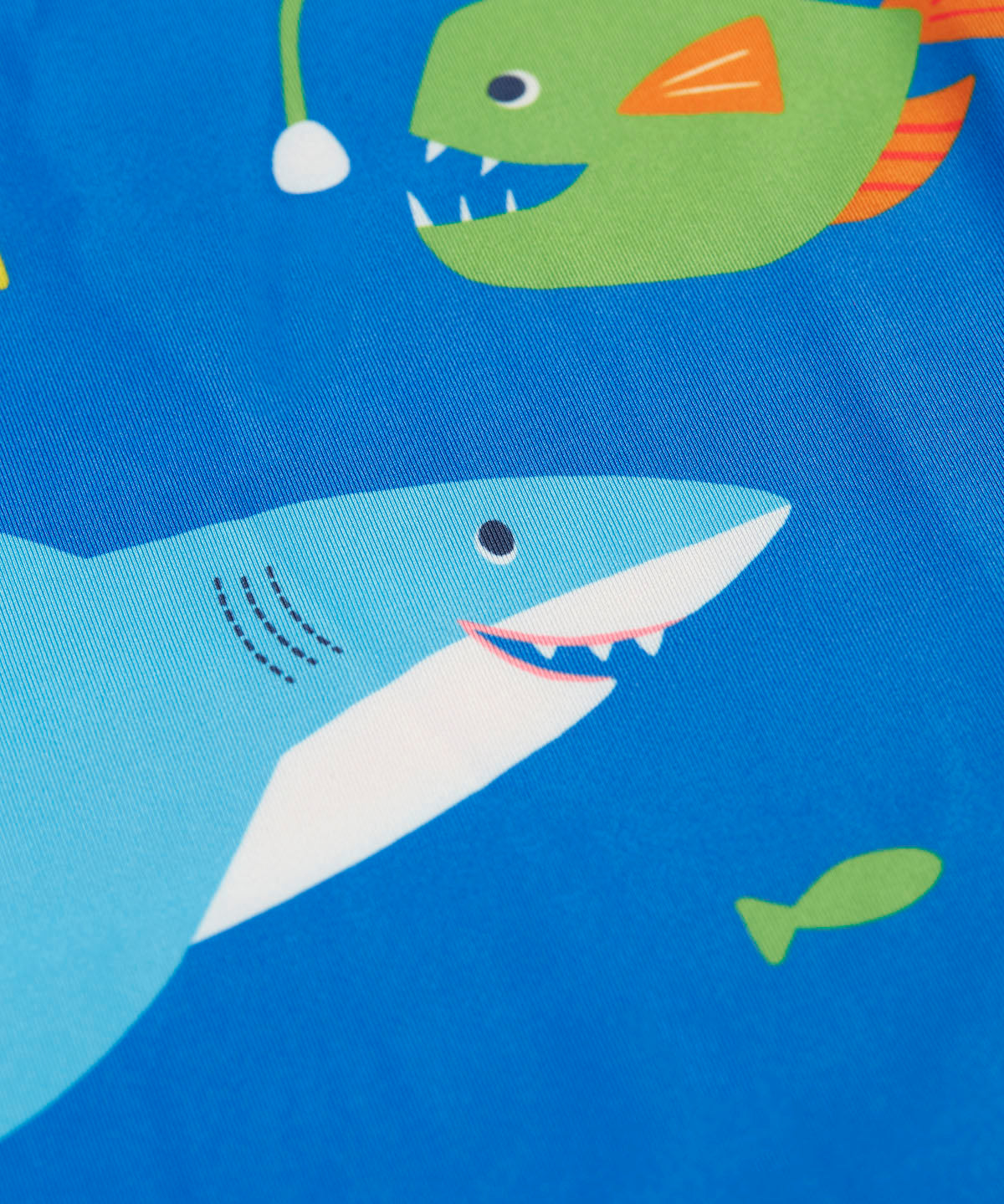 A close up of the shark and angler fish design on the blue Frugi rash vest laid flat.