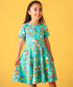 Child smiling and standing in front of a light orange background. Wearing the turquoise skater dress with repeating roller blades and skateboard prints.