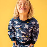 Child smiling and standing in front of a orange background. Wearing a dark blue sweatshirt and navy trim with a repeating manta ray print